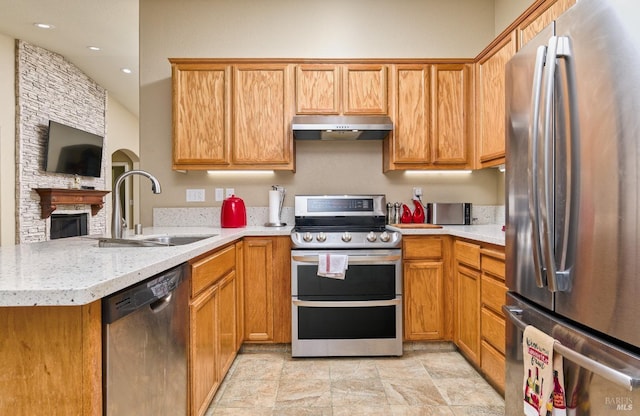 kitchen featuring appliances with stainless steel finishes, open floor plan, a sink, a peninsula, and under cabinet range hood