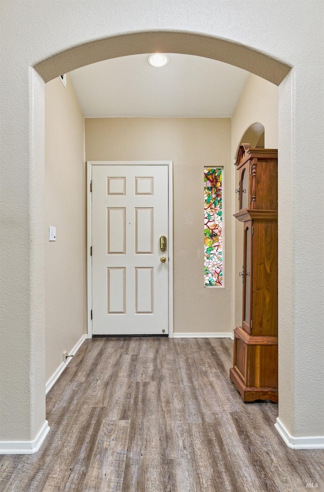 entrance foyer featuring arched walkways, baseboards, and wood finished floors