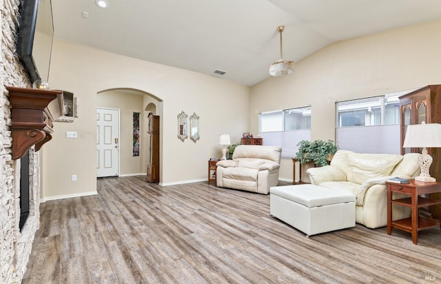 living room with arched walkways, visible vents, light wood-style floors, vaulted ceiling, and baseboards