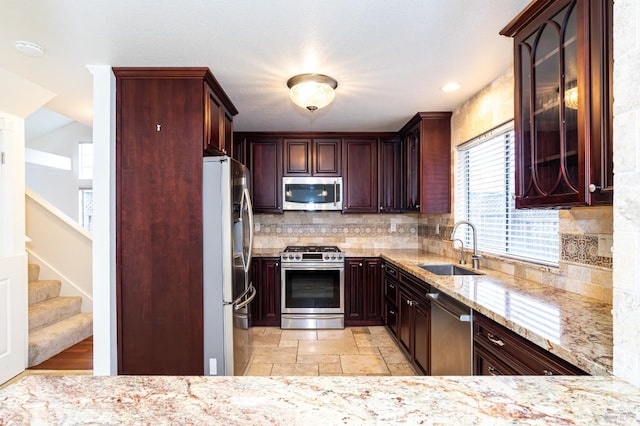 kitchen featuring stone tile floors, appliances with stainless steel finishes, light stone counters, a sink, and backsplash