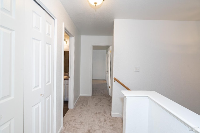 hall with baseboards, light colored carpet, a textured ceiling, and an upstairs landing