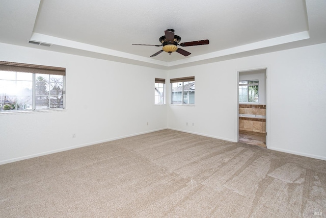 empty room featuring a wealth of natural light, a tray ceiling, and visible vents