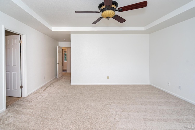 empty room with light carpet, baseboards, a raised ceiling, and a ceiling fan