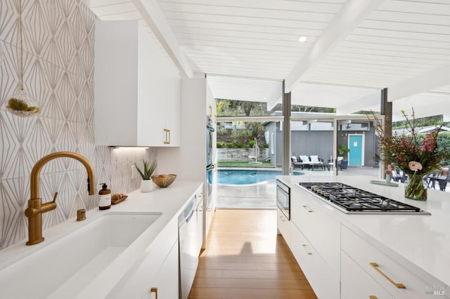 kitchen featuring a sink, white cabinets, light countertops, appliances with stainless steel finishes, and beamed ceiling