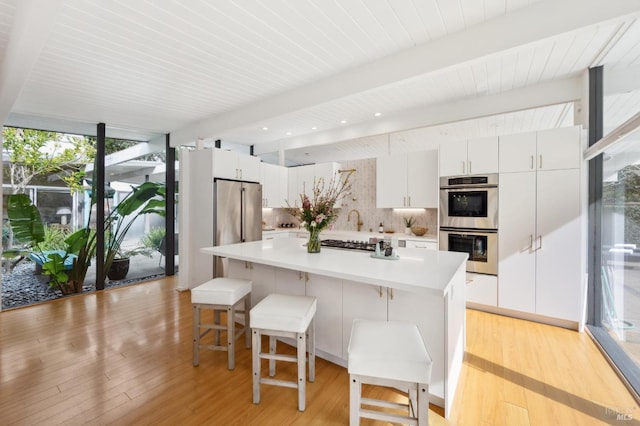 kitchen with light wood-style flooring, appliances with stainless steel finishes, backsplash, floor to ceiling windows, and beamed ceiling