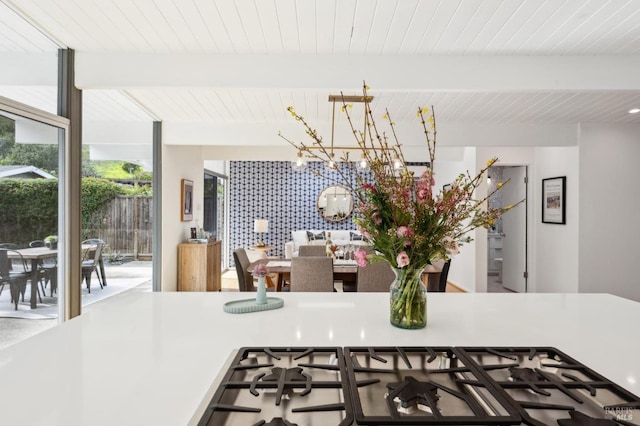 kitchen with wooden ceiling, a notable chandelier, stainless steel gas cooktop, beam ceiling, and a wall of windows