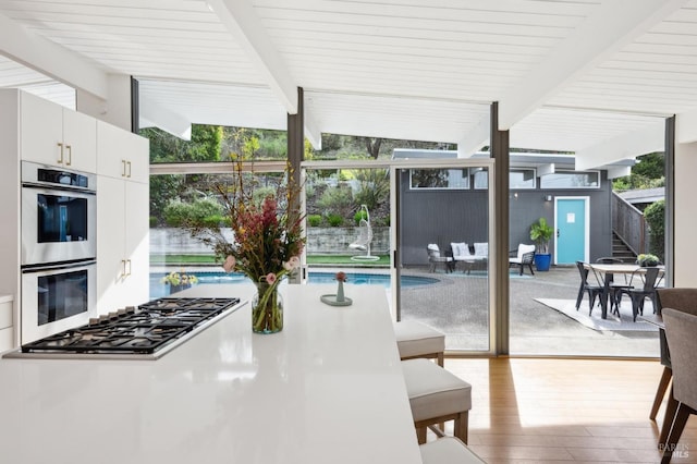 interior space featuring lofted ceiling with beams, appliances with stainless steel finishes, wood finished floors, and floor to ceiling windows