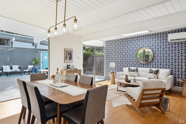 dining room featuring a wall mounted air conditioner, beamed ceiling, light wood finished floors, and wallpapered walls