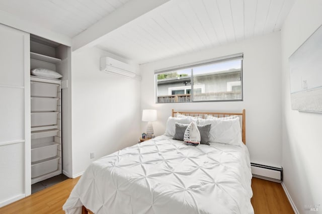 bedroom with a baseboard radiator, wood finished floors, baseboards, beamed ceiling, and a wall mounted air conditioner