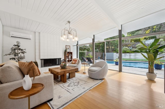 living area featuring a notable chandelier, a fireplace, a wall mounted AC, wood finished floors, and a wall of windows