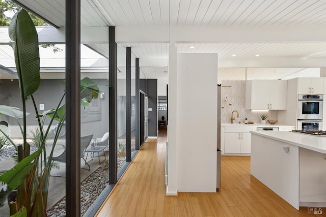 interior space with tasteful backsplash, light countertops, double oven, light wood-style floors, and a sink