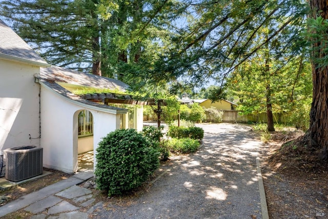 view of side of property with a shingled roof, fence, central AC, and stucco siding