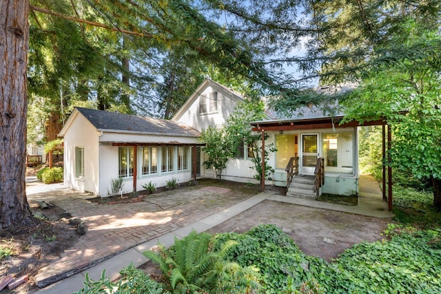 back of property featuring a patio, a porch, roof with shingles, and stucco siding