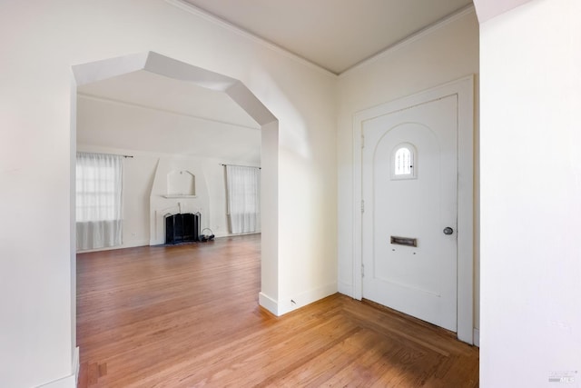 entrance foyer with ornamental molding, a large fireplace, baseboards, and wood finished floors