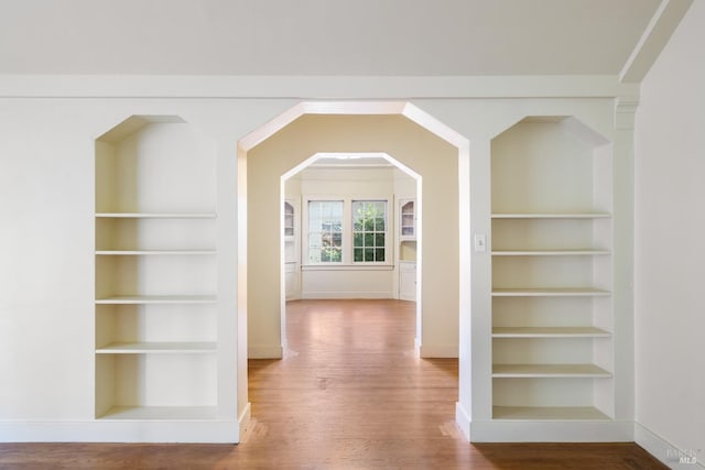 hall featuring built in shelves, wood finished floors, and baseboards