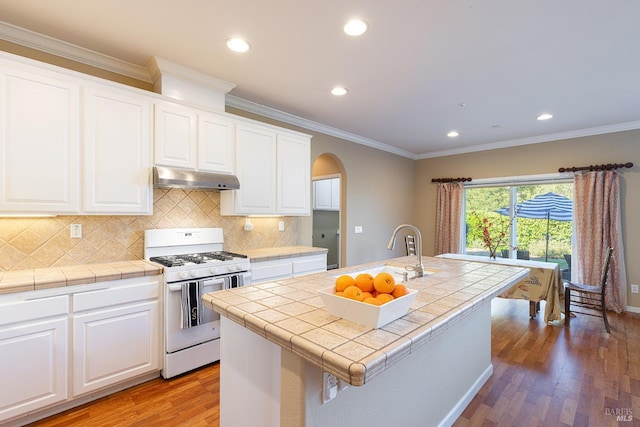 kitchen featuring arched walkways, white gas stove, under cabinet range hood, a sink, and tile counters