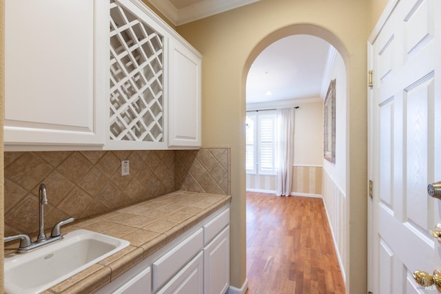 kitchen featuring crown molding, arched walkways, white cabinets, and a sink