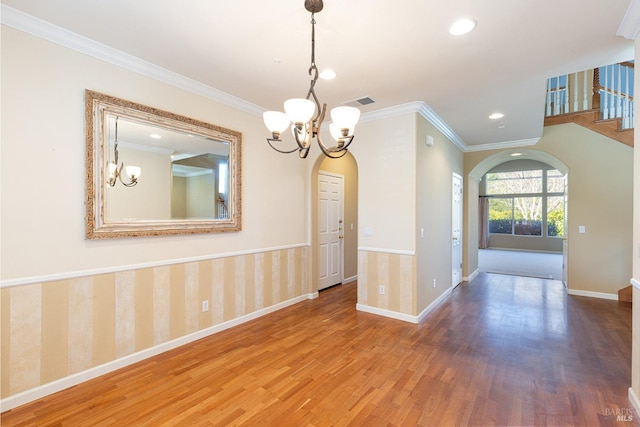 unfurnished dining area with arched walkways, a notable chandelier, wood finished floors, baseboards, and wallpapered walls