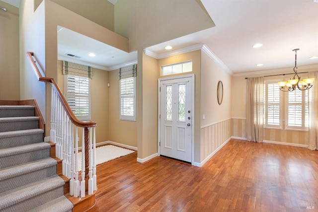 entrance foyer with a notable chandelier, ornamental molding, a wealth of natural light, and wood finished floors