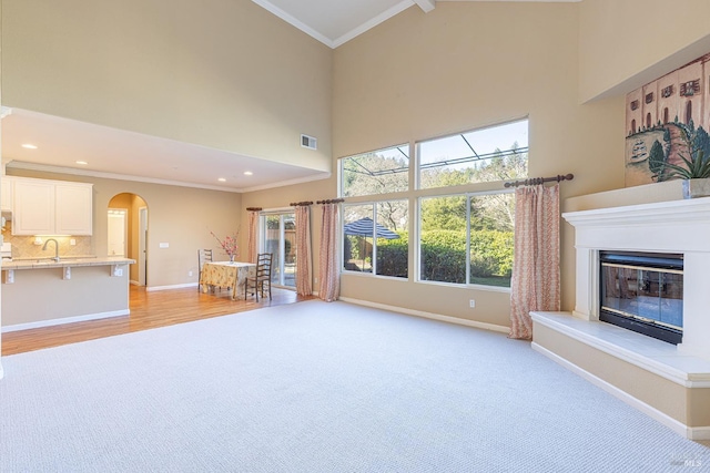 unfurnished living room featuring arched walkways, visible vents, baseboards, a glass covered fireplace, and crown molding