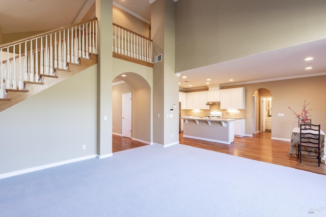 unfurnished living room with arched walkways, ornamental molding, visible vents, and baseboards