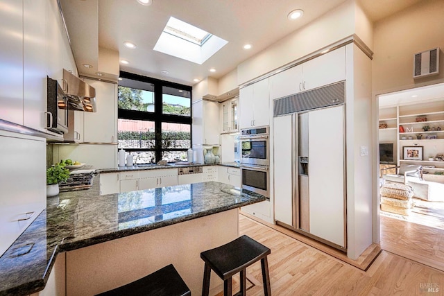 kitchen with paneled built in refrigerator, a peninsula, double oven, and white cabinetry