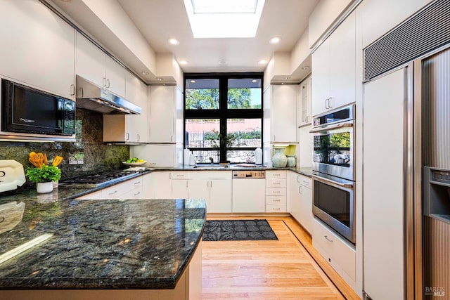 kitchen featuring a skylight, white cabinets, built in appliances, a peninsula, and under cabinet range hood