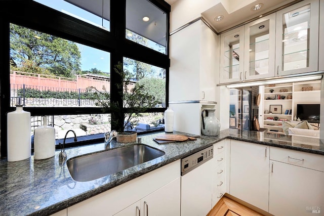 kitchen with white dishwasher, glass insert cabinets, white cabinets, and a sink