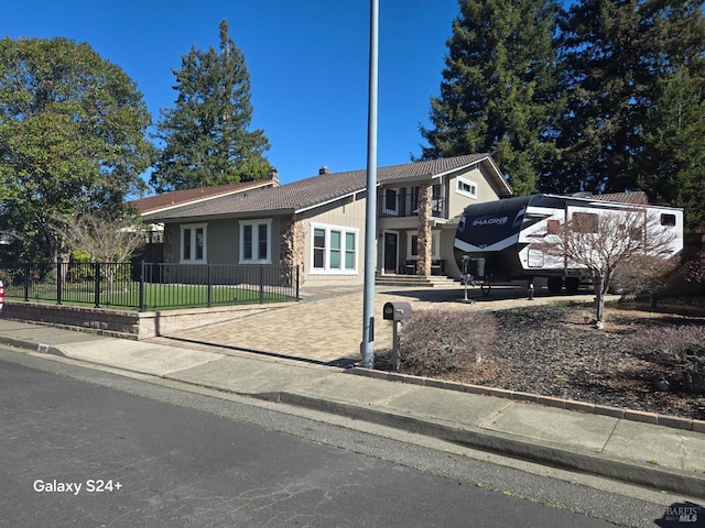 view of front facade with driveway, a fenced front yard, and a tile roof