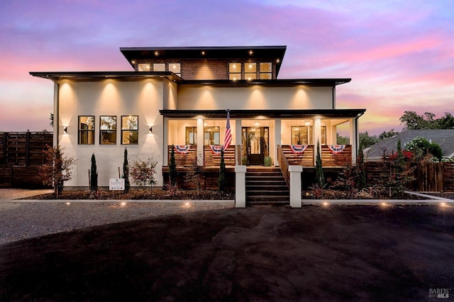 view of front facade featuring a porch, fence, stairway, and stucco siding