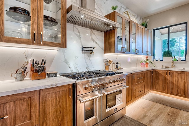 kitchen with a sink, double oven range, brown cabinets, range hood, and glass insert cabinets