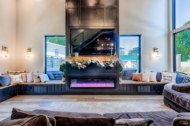 living room featuring a towering ceiling, light wood-type flooring, visible vents, and a glass covered fireplace