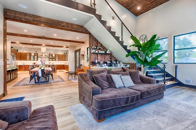 living area with light wood finished floors, baseboards, stairway, and beam ceiling