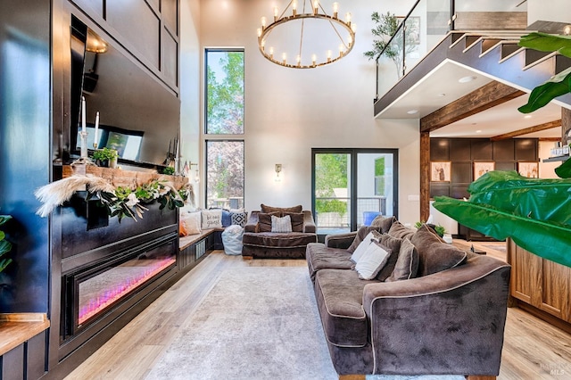 living area with a chandelier, a towering ceiling, a wealth of natural light, and light wood-style floors