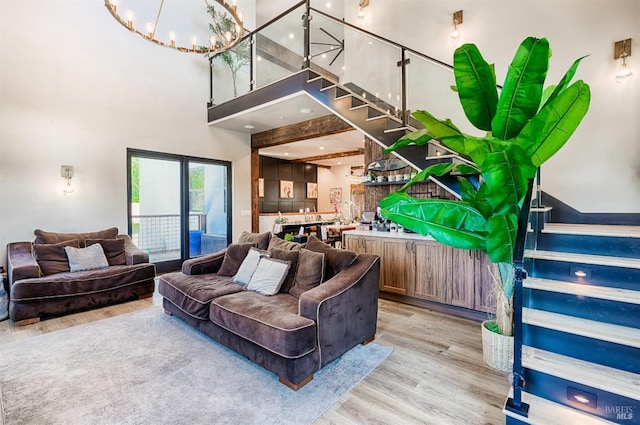 living area with a towering ceiling, light wood-style flooring, stairs, and a notable chandelier