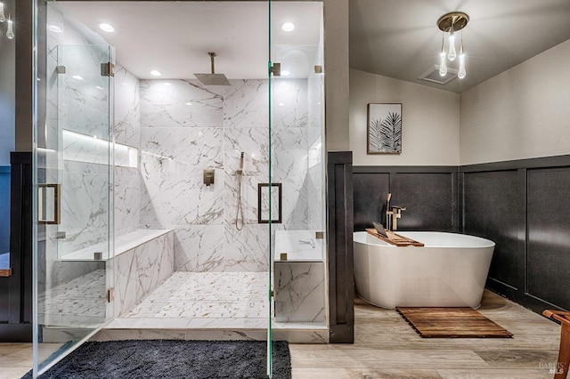 bathroom with a marble finish shower, a decorative wall, wainscoting, wood finished floors, and a freestanding tub