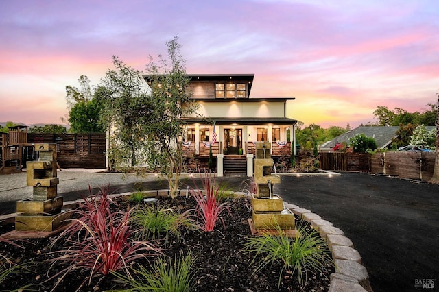 back of property at dusk featuring a fenced front yard and a porch