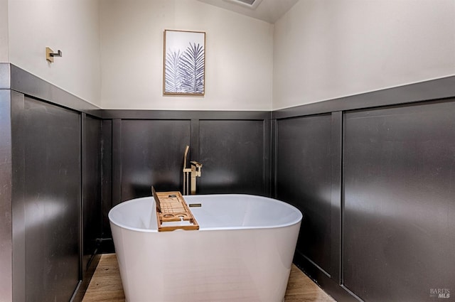 full bath featuring a freestanding tub, a decorative wall, and wood finished floors