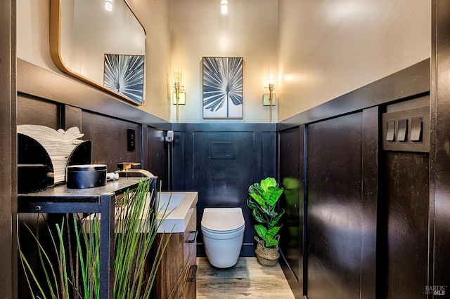 bathroom featuring a wainscoted wall, a decorative wall, toilet, and wood finished floors