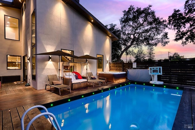 pool at dusk with a hot tub, a fenced backyard, a deck, and a fenced in pool