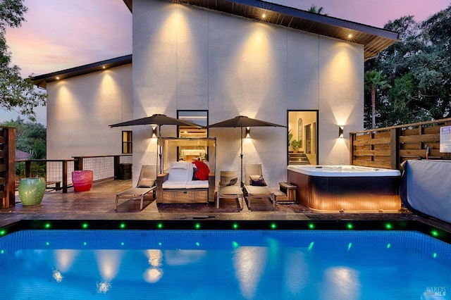 back of property at dusk with a pool, a hot tub, a wooden deck, and stucco siding