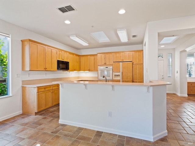 kitchen featuring black microwave, built in fridge, a breakfast bar, a skylight, and visible vents