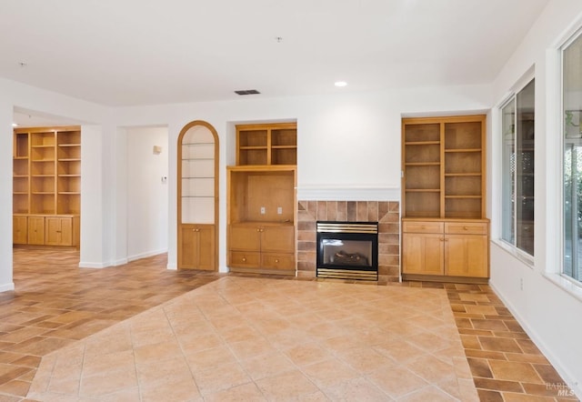 unfurnished living room with light tile patterned floors, visible vents, baseboards, built in features, and a tiled fireplace