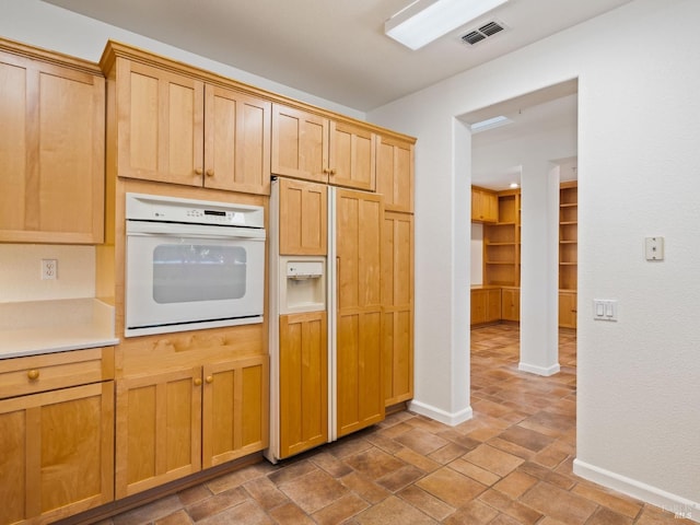 kitchen with white oven, light countertops, visible vents, paneled built in fridge, and baseboards