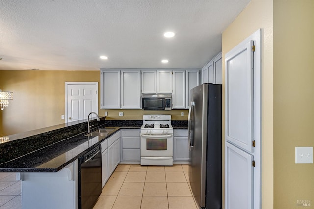 kitchen featuring appliances with stainless steel finishes, white cabinetry, a sink, dark stone countertops, and a peninsula