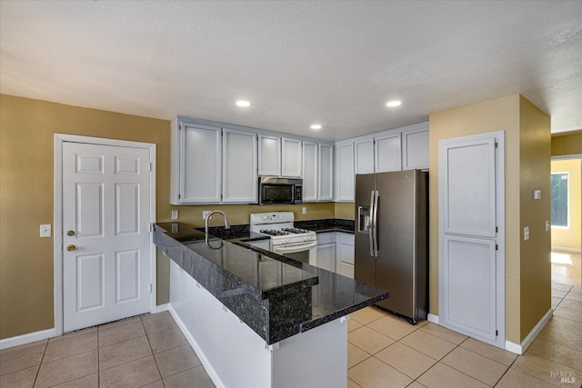 kitchen with light tile patterned flooring, stainless steel appliances, a peninsula, white cabinetry, and baseboards