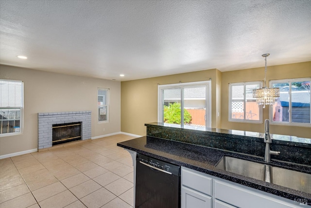 kitchen featuring a sink, white cabinets, black dishwasher, hanging light fixtures, and a brick fireplace