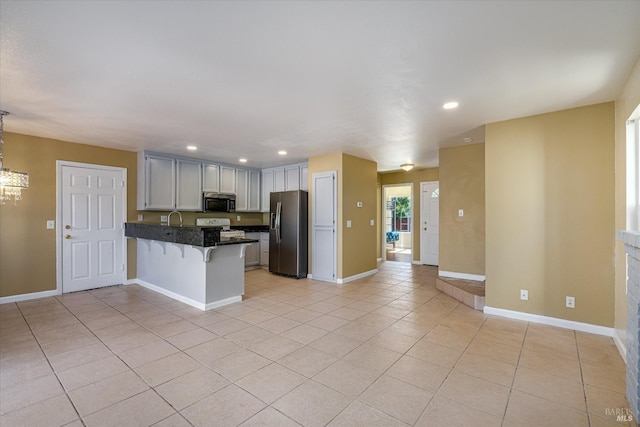 kitchen with light tile patterned floors, a peninsula, a kitchen breakfast bar, appliances with stainless steel finishes, and dark countertops