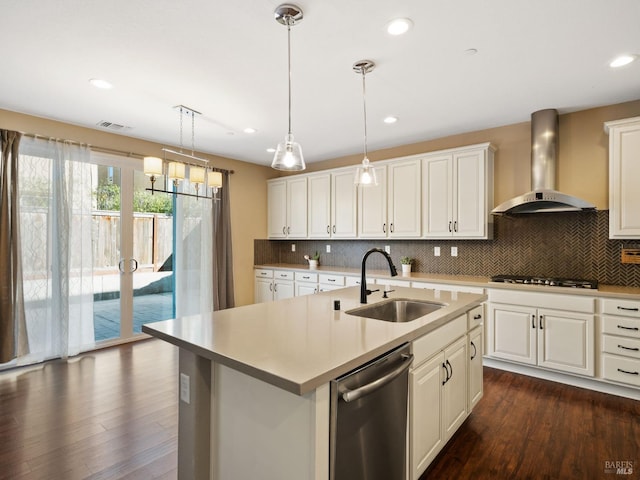 kitchen with stainless steel appliances, a sink, light countertops, wall chimney range hood, and an island with sink