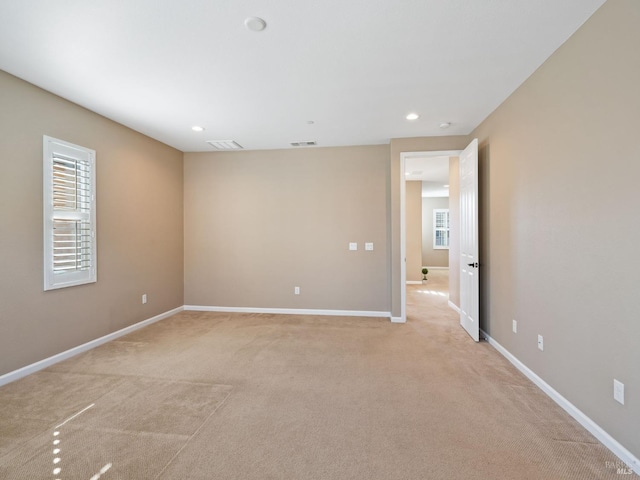 spare room featuring baseboards, a healthy amount of sunlight, visible vents, and light colored carpet